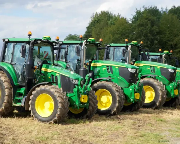 Rząd zielonych traktorów John Deere z żółtymi felgami na polu. Widać ich charakterystyczny wygląd i potężne opony.