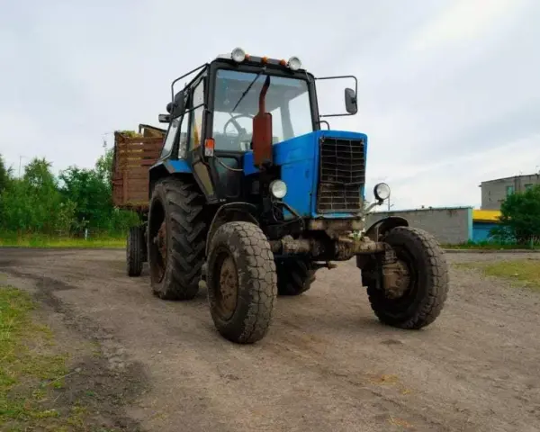 Niebieski traktor z przyczepą na tle wiejskiego krajobrazu. Zastanawiasz się, ile zarabia traktorzysta?
