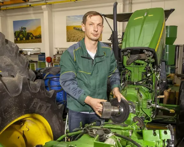 Mechanik z częścią John Deere, być może szuka informacji o john deere kody serwisowe, aby naprawić traktor.