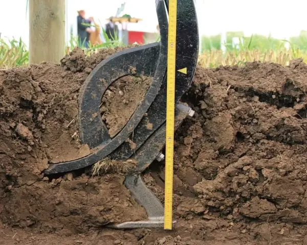 Czarne, metalowe elementy podeszwy płużnej zagłębiają się w ziemi. Obok miarka pokazuje głębokość orki.