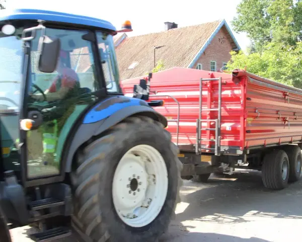Operator traktora w czerwonej koszulce prowadzi maszynę z przyczepą.