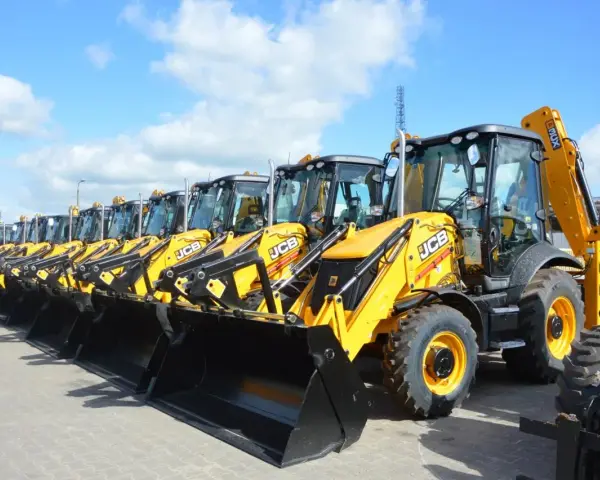 Rząd żółtych koparko-ładowarek JCB stoi na placu.
