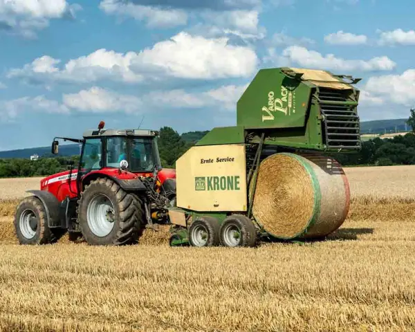 Czerwony traktor Massey Ferguson 6180 z prasą Krone Vario Pack na polu. Dane techniczne tej maszyny pozwalają na efektywne belowanie.