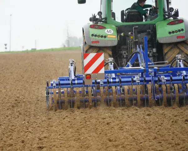 Zielony traktor z agregatem uprawowym, który przygotowuje pole. Różne rodzaje wałów uprawowych pomagają w tym procesie.