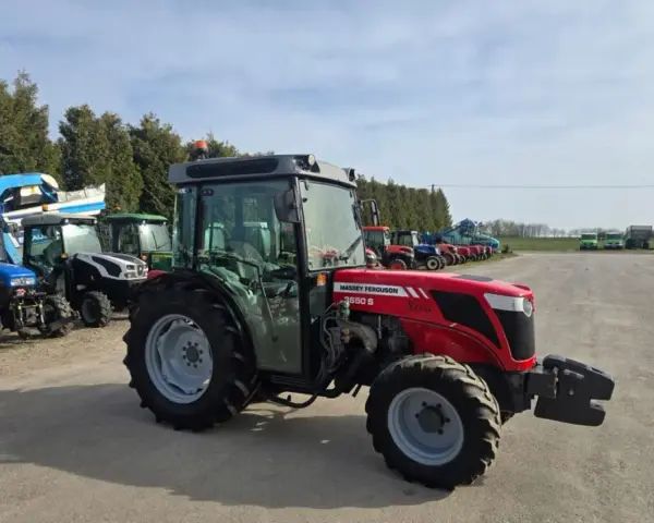 Czerwony ciągnik Massey Ferguson 3650 S Xtra, z kabiną, zaparkowany na placu z innymi maszynami. Dane techniczne tego modelu są imponujące.
