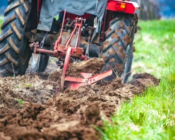 Czerwony traktor z pługiem orze pole, przygotowując ziemię pod zasiew. Rolnictwo w akcji.