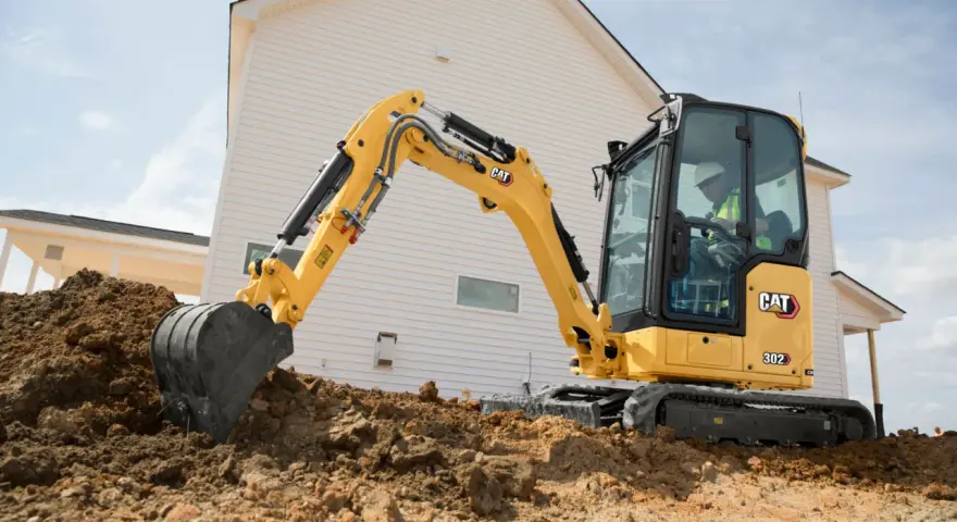 Żółta koparka gąsienicowa Caterpillar 302 CR pracuje na budowie domu, kopiąc ziemię.