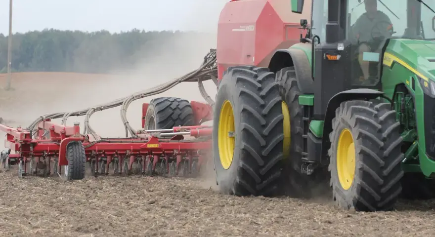 Zielony traktor z siewnikiem Horsch pracuje na polu. Trwa czas orki 1 ha, widać kurz unoszący się z ziemi.