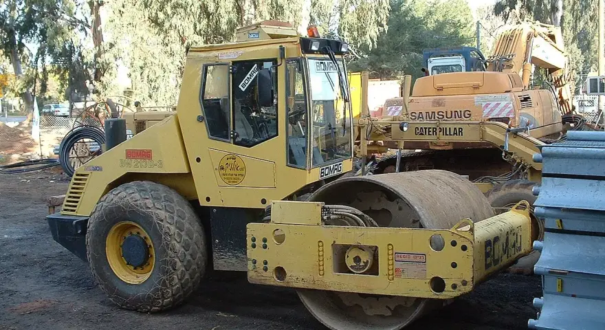Żółty walec drogowy BOMAG BW 213D-3 gotowy do budowy drogi. W tle koparka Samsung Caterpillar.