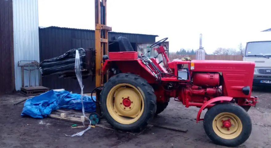 Czerwony traktor z ładowarką czołową, gotowy do pracy. Może posłużyć do budowy masztu do ciągnika.