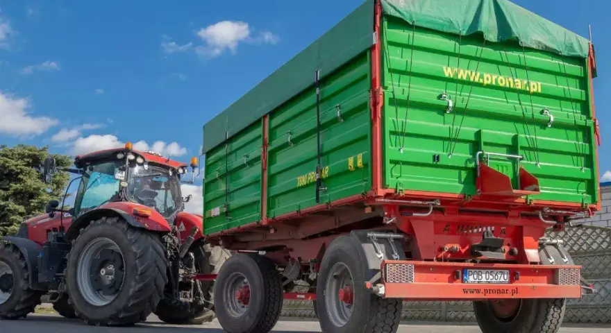 Czerwony traktor z zieloną przyczepą rolniczą. Czy przyczepa rolnicza musi być zarejestrowana? Sprawdź przepisy!