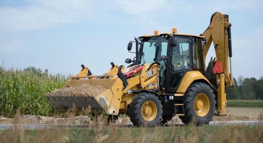 Żółta koparko-ładowarka CAT 432 w trakcie budowy drogi, z pełną łyżką ziemi.