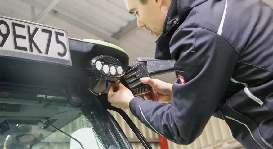 Mężczyzna montuje lampy LED na ciągniku. Dowiedz się, jak podłączyć lampy LED w ciągniku, aby poprawić widoczność w nocy.