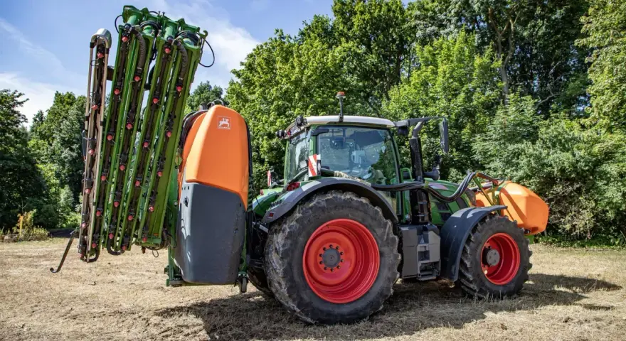 Zielony traktor z zamontowanym opryskiwaczem polowym, gotowy do pracy.