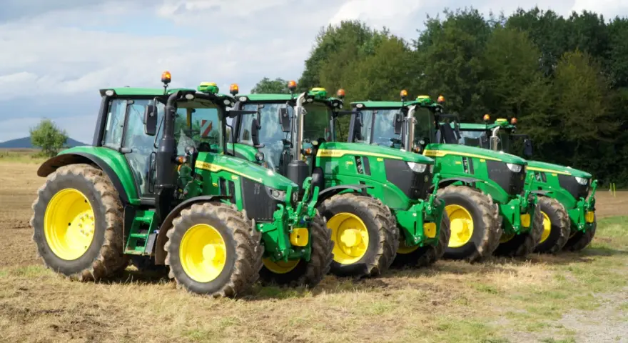 Rząd zielonych traktorów John Deere z żółtymi felgami na polu. Widać ich charakterystyczny wygląd i potężne opony.
