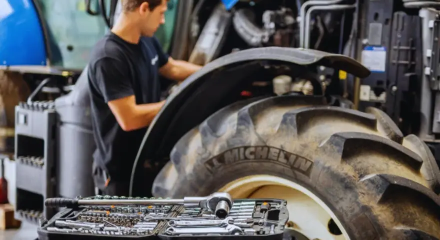Mechanik pracuje przy traktorze, a obok leży walizka z narzędziami. Kluczowe dla sprawnej konserwacji maszyn rolniczych są regularne przeglądy.