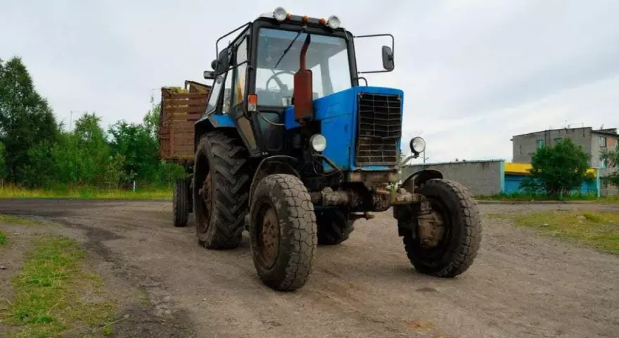 Niebieski traktor z przyczepą na tle wiejskiego krajobrazu. Zastanawiasz się, ile zarabia traktorzysta?