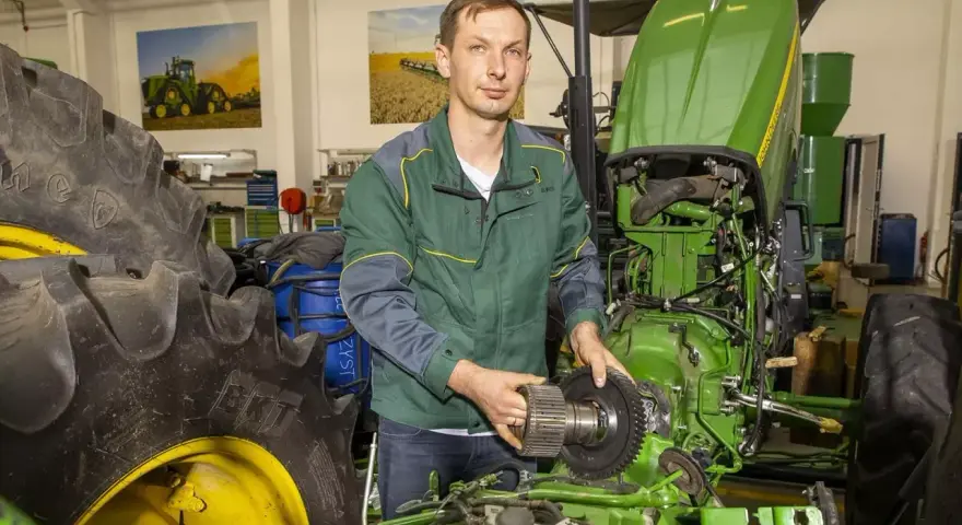 Mechanik z częścią John Deere, być może szuka informacji o john deere kody serwisowe, aby naprawić traktor.