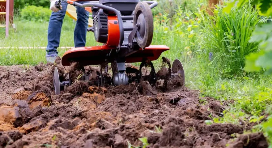Mężczyzna pracuje glebogryzarką samoróbką, spulchniając ziemię w ogrodzie.