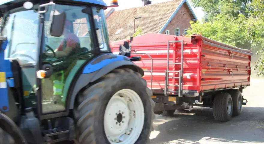 Operator traktora w czerwonej koszulce prowadzi maszynę z przyczepą.