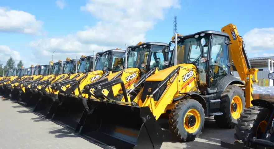 Rząd żółtych koparko-ładowarek JCB stoi na placu.