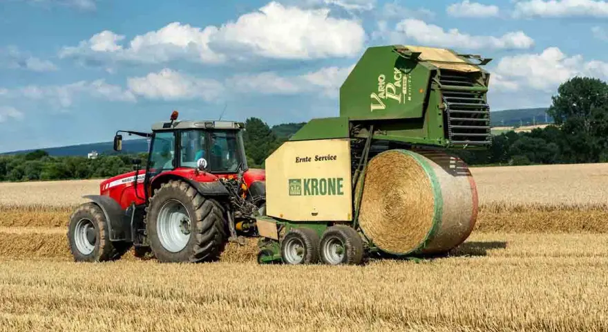 Czerwony traktor Massey Ferguson 6180 z prasą Krone Vario Pack na polu. Dane techniczne tej maszyny pozwalają na efektywne belowanie.