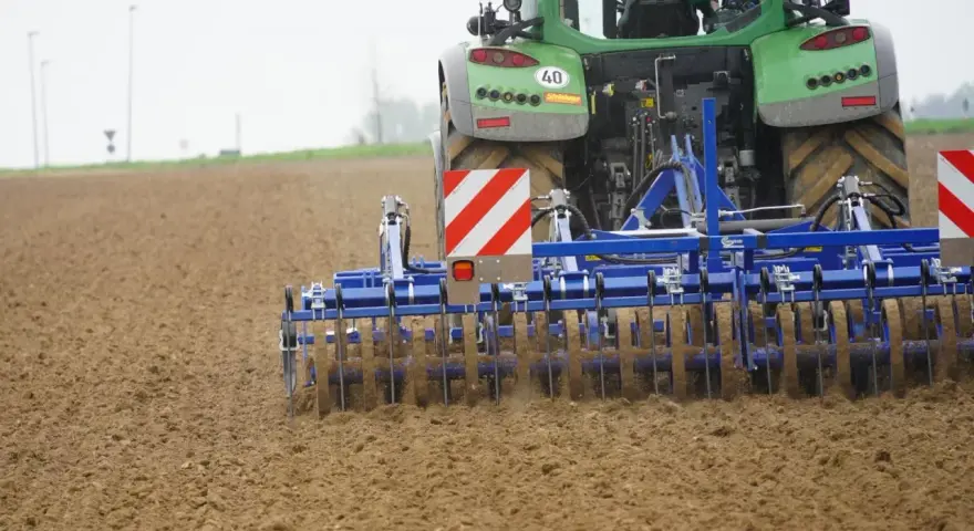Zielony traktor z agregatem uprawowym, który przygotowuje pole. Różne rodzaje wałów uprawowych pomagają w tym procesie.