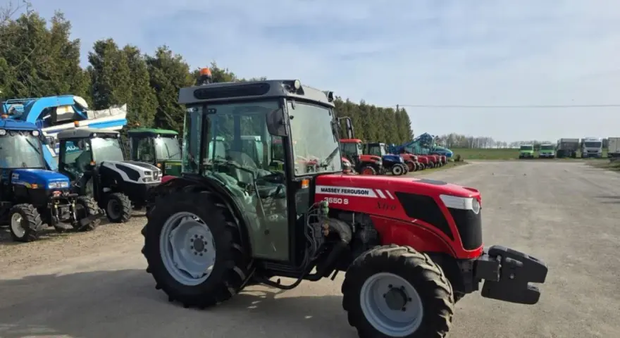 Czerwony ciągnik Massey Ferguson 3650 S Xtra, z kabiną, zaparkowany na placu z innymi maszynami. Dane techniczne tego modelu są imponujące.