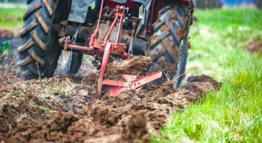 Czerwony traktor z pługiem orze pole, przygotowując ziemię pod zasiew. Rolnictwo w akcji.