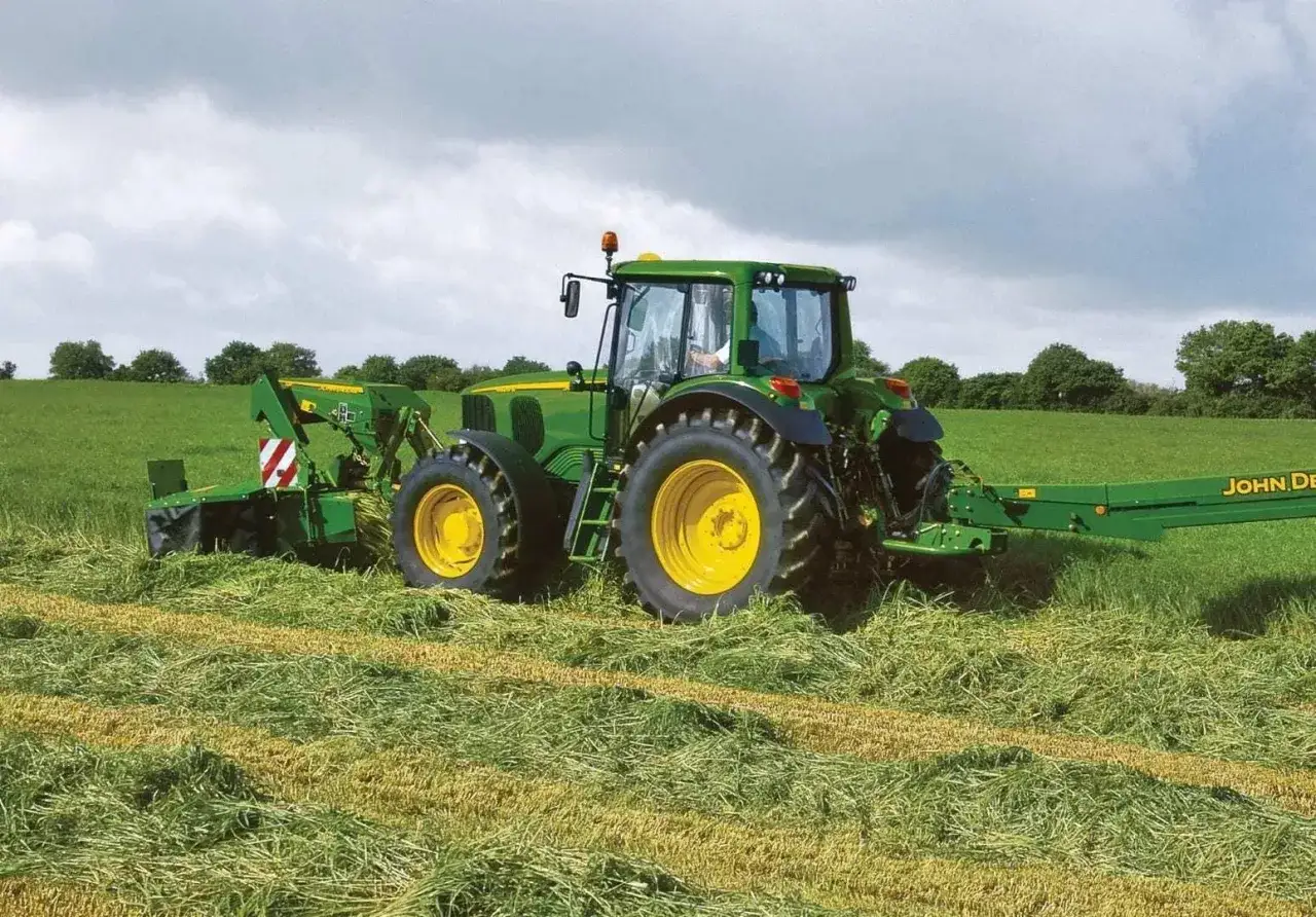 Zielony traktor John Deere 6820 z kosiarką pracuje na polu. Dane techniczne tego modelu są imponujące.