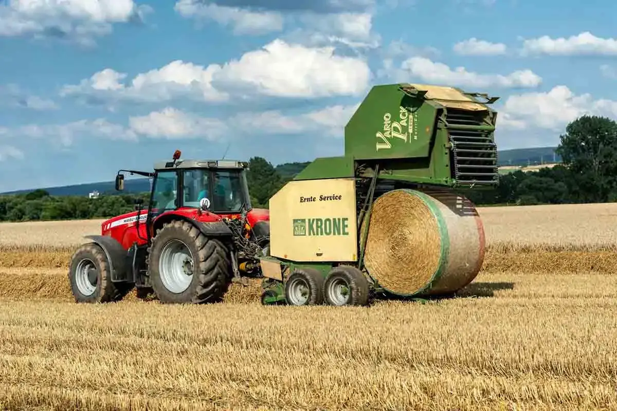 Czerwony ciągnik Massey Ferguson 6180 z prasą Krone Vario Pack zbiera siano na polu.