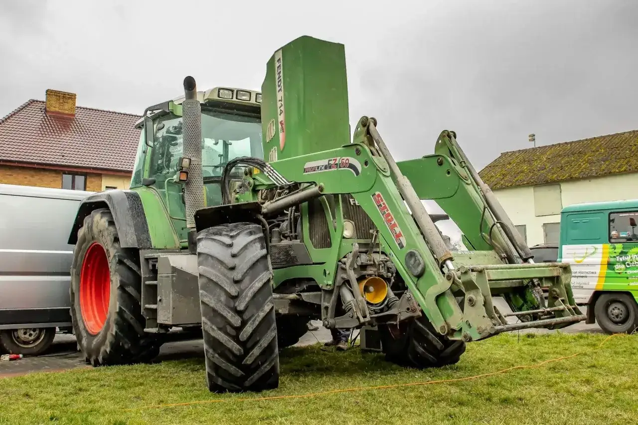 Zielony ciągnik Fendt 714 Vario z ładowaczem czołowym. Dane techniczne tego modelu są imponujące, co widać po jego solidnej budowie.