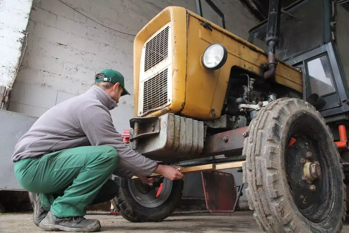 Mężczyzna w zielonych spodniach i czapce reguluje przednie koło ż&oacute;łtego ciągnika 4x4, aby ustawić zbieżność.