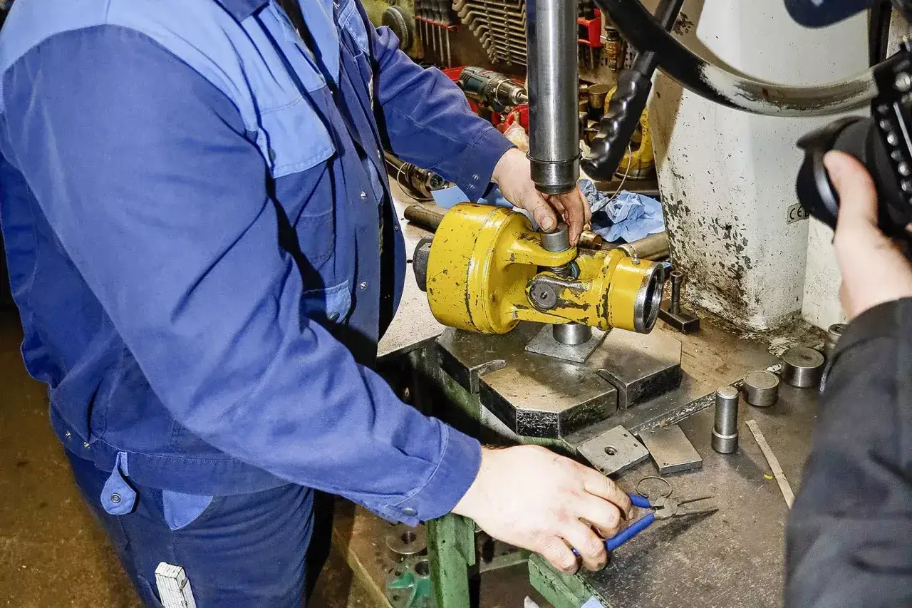 Mechanik w niebieskim kombinezonie pracuje nad ż&oacute;łtym wałem cardana, przygotowując go do montażu.
