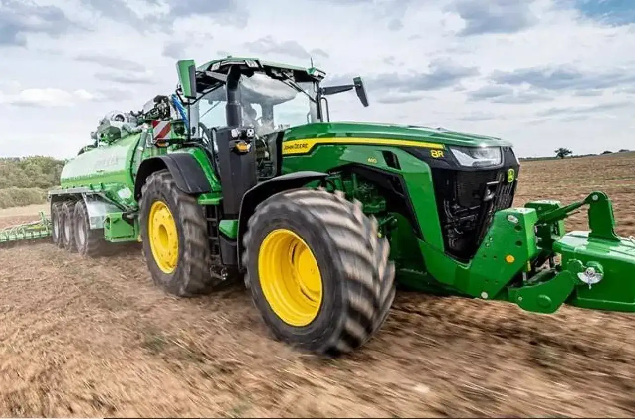 Potężny zielony traktor marki John Deere z przyczepą asenizacyjną pracuje na polu.