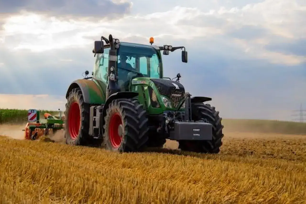 Zielony traktor orze pole. Dobre ubezpieczenie ciągnika rolniczego to podstawa spokojnej pracy.