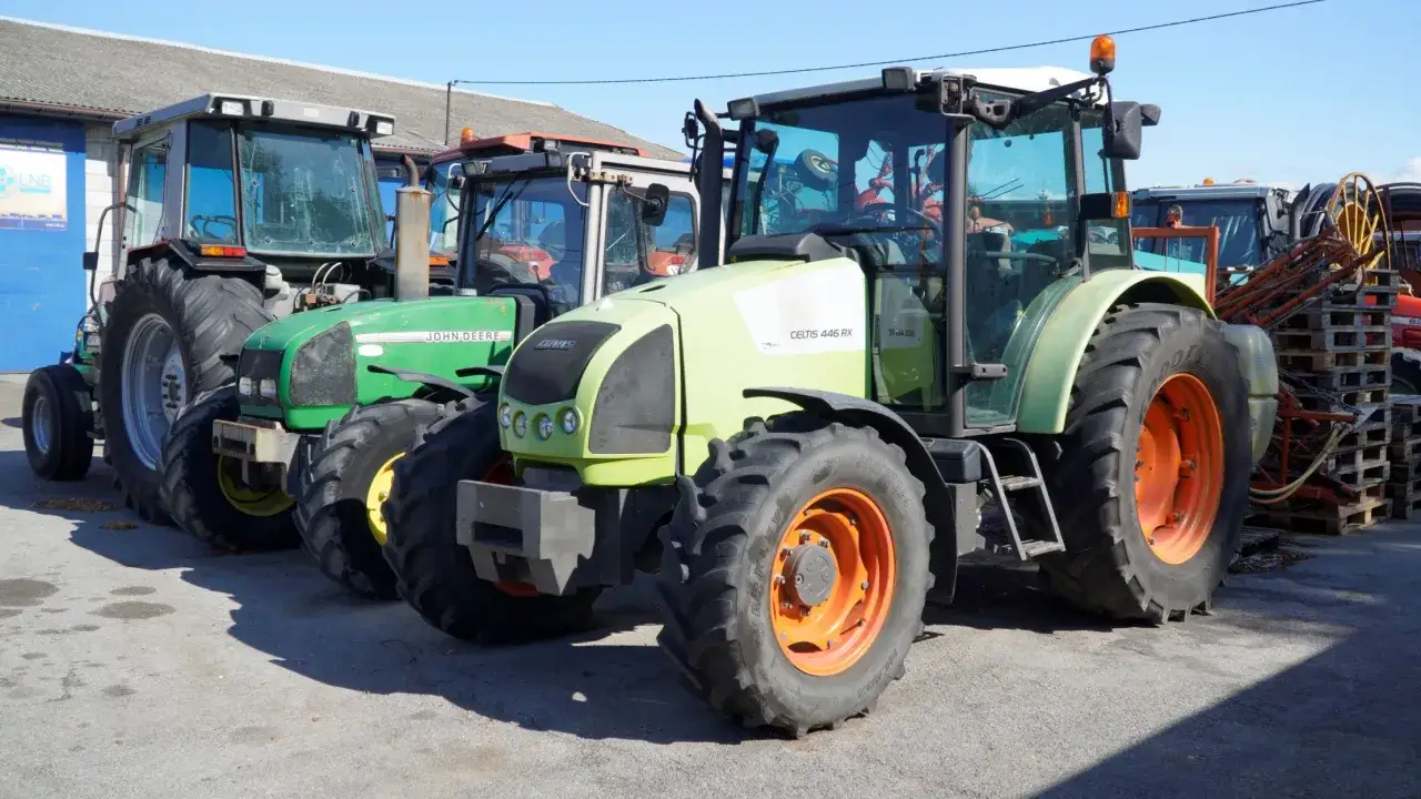 Ciągniki rolnicze, w tym zielony John Deere i jasnoszary Claas Celtis 446 RX, stoją zaparkowane. Zastanawiasz się, ile motogodzin wytrzyma ciągnik?