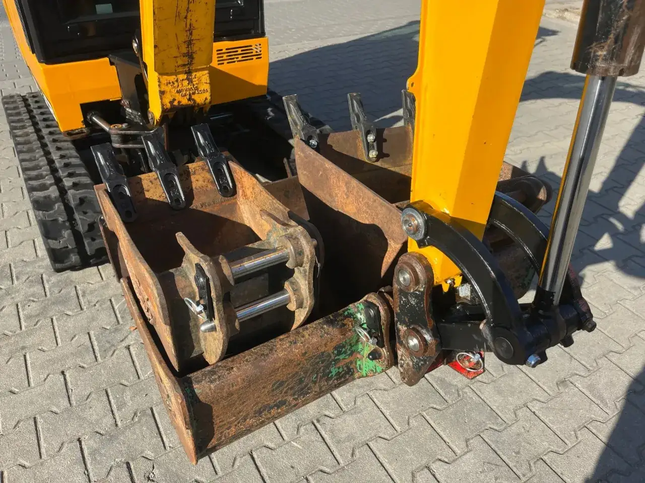 Ż&oacute;łta koparka z gąsienicami i zamontowanym osprzętem. Widać szerokość koparki i jej mechanizmy.