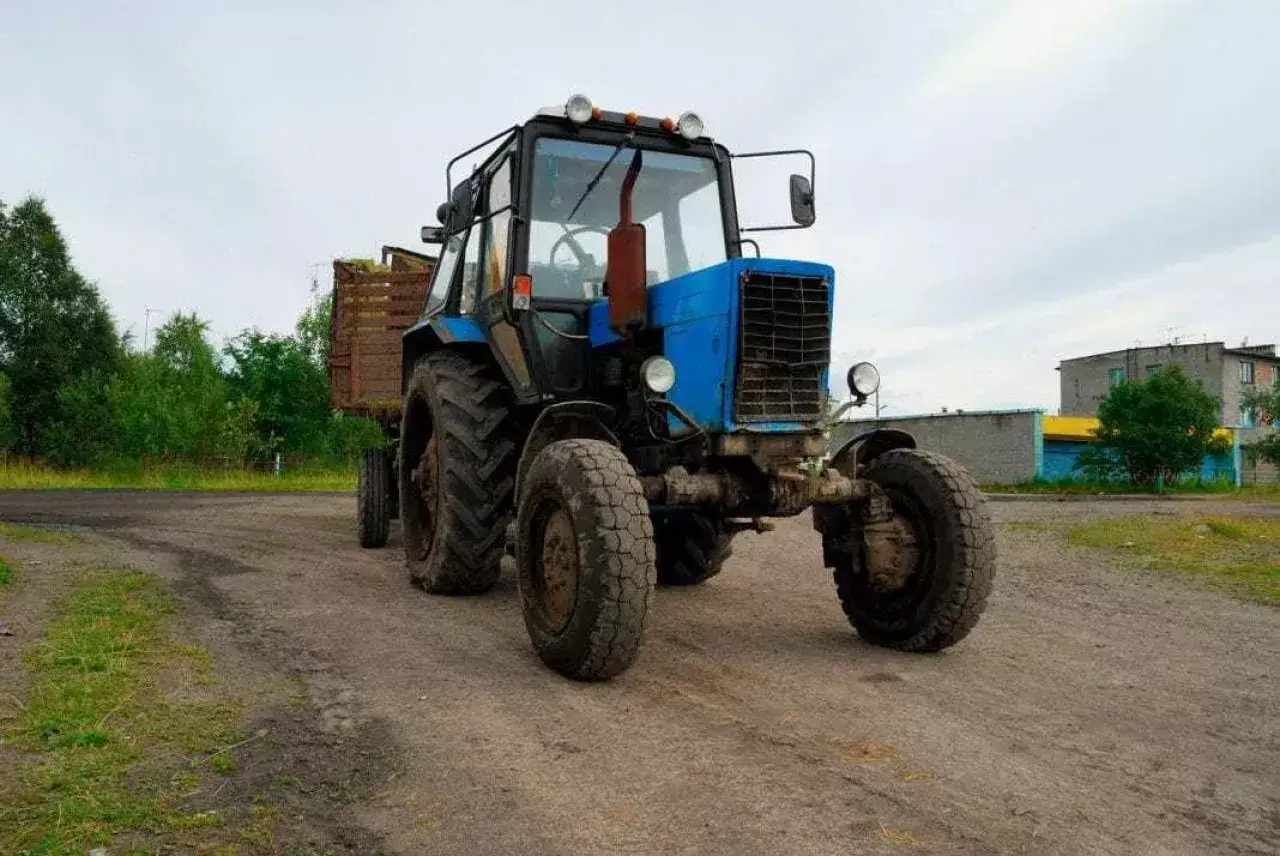 Niebieski traktor z przyczepą pełną zielonki. Zastanawiasz się, ile zarabia traktorzysta?