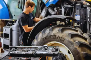 Mechanik pracuje przy traktorze, a obok leży walizka z narzędziami. Kluczowe dla sprawnej konserwacji maszyn rolniczych są regularne przeglądy.