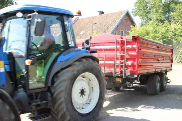 Operator traktora w czerwonej koszulce prowadzi maszynę z przyczepą.