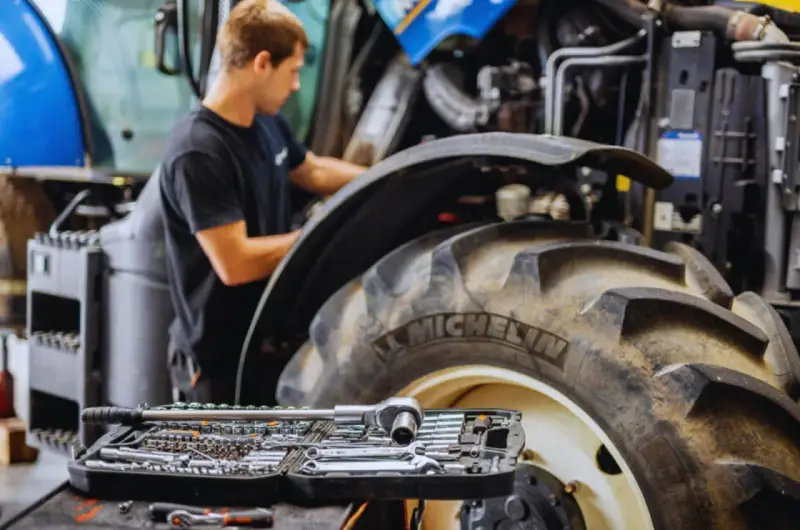 Mechanik pracuje przy traktorze, a obok leży walizka z narzędziami. Kluczowe dla sprawnej konserwacji maszyn rolniczych są regularne przeglądy.